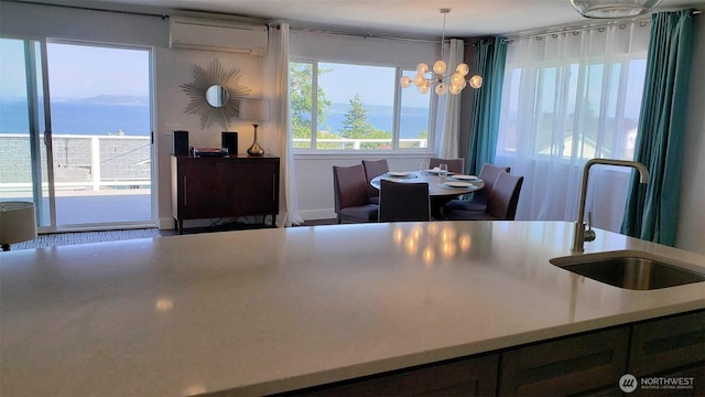 kitchen featuring light countertops, a wall mounted AC, a sink, a notable chandelier, and hanging light fixtures