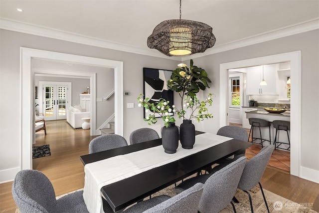 dining room with an inviting chandelier, ornamental molding, wood finished floors, and stairway