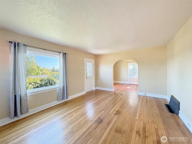 unfurnished living room featuring a textured ceiling, wood-type flooring, arched walkways, and a healthy amount of sunlight