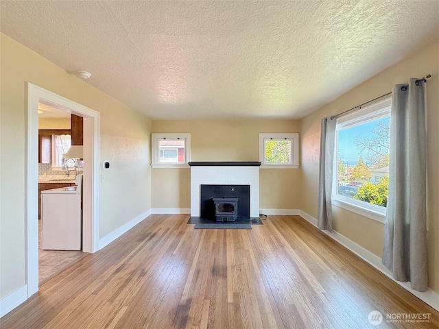 unfurnished living room with a wood stove, light wood-style flooring, a textured ceiling, and baseboards