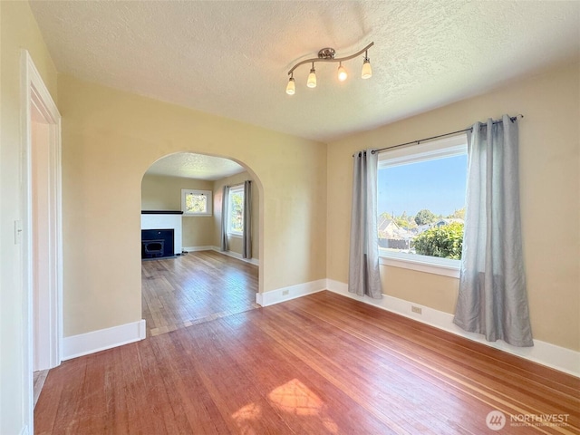 spare room featuring arched walkways, plenty of natural light, a textured ceiling, and wood finished floors