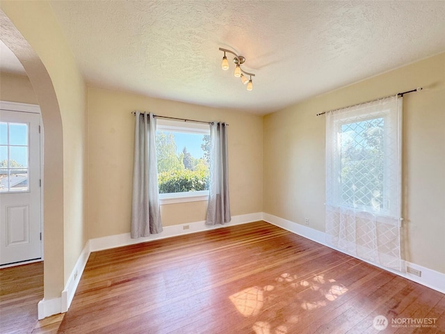 unfurnished room with a wealth of natural light, wood finished floors, arched walkways, and a textured ceiling