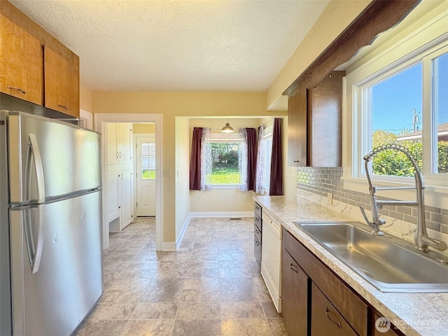 kitchen featuring freestanding refrigerator, baseboards, a sink, decorative backsplash, and light countertops
