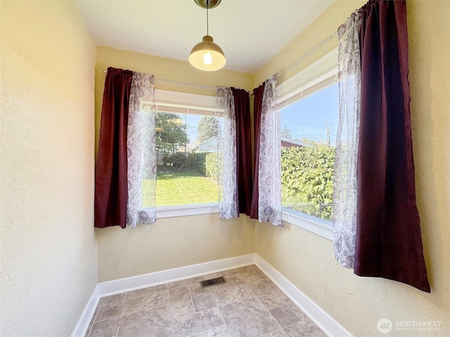 unfurnished dining area with a textured wall, a wealth of natural light, baseboards, and visible vents