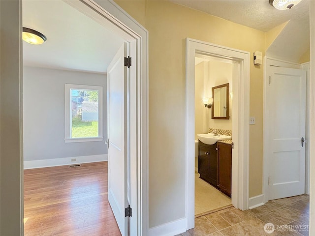 hallway featuring baseboards, light wood finished floors, and a sink