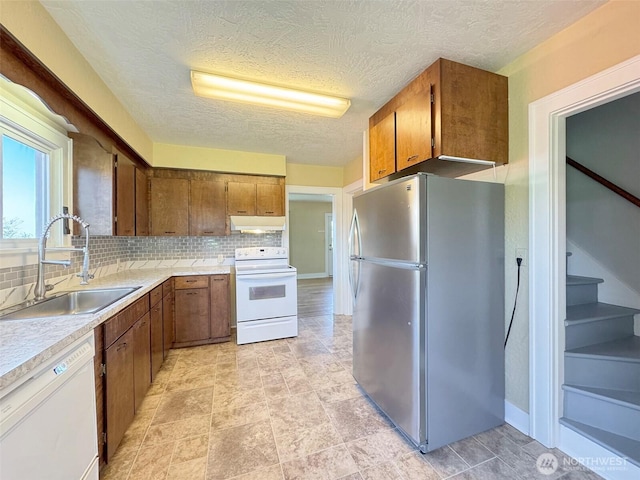 kitchen featuring under cabinet range hood, brown cabinets, a sink, and white appliances