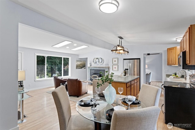 dining room with light wood-type flooring, baseboards, a brick fireplace, and lofted ceiling