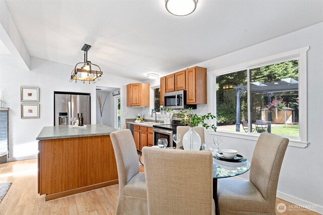 dining area with baseboards, vaulted ceiling, and light wood-style floors