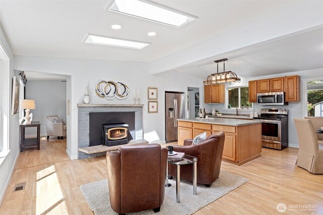 living area with vaulted ceiling with beams, a wood stove, light wood finished floors, and visible vents