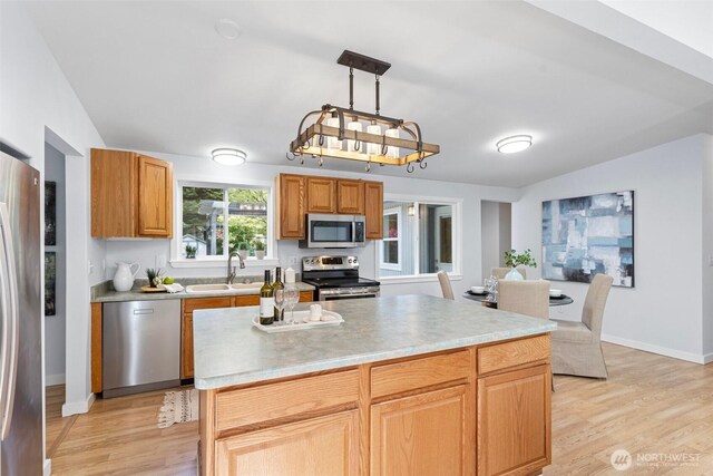 kitchen featuring appliances with stainless steel finishes, a sink, light countertops, light wood-style flooring, and baseboards