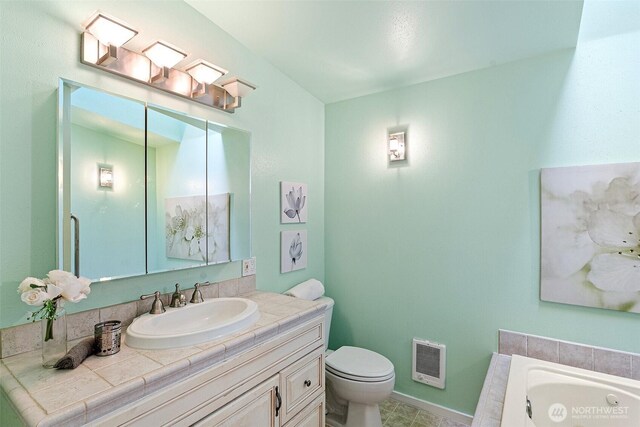bathroom featuring vanity, toilet, baseboards, heating unit, and a tub with jets