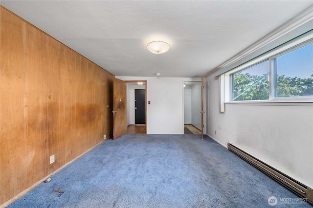 unfurnished room with wooden walls, baseboard heating, and carpet