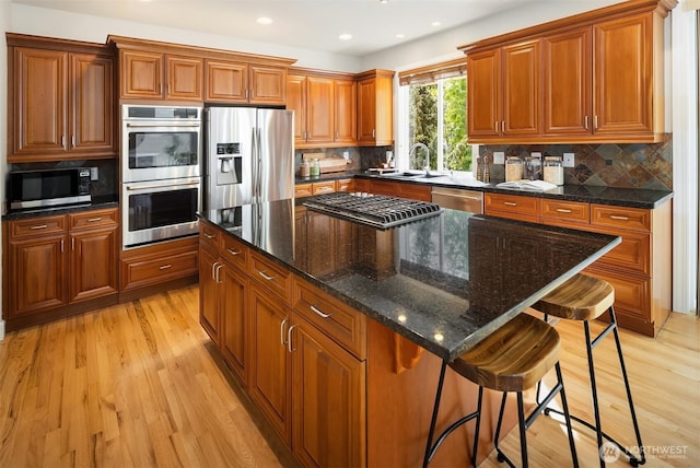 kitchen featuring stainless steel appliances, brown cabinets, light wood finished floors, a sink, and a breakfast bar