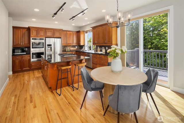 kitchen featuring appliances with stainless steel finishes, a kitchen island, brown cabinetry, a chandelier, and baseboards