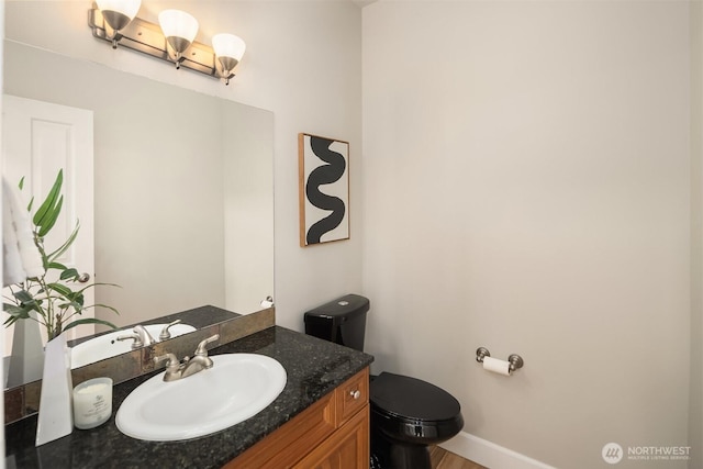 half bathroom featuring wood finished floors, baseboards, vanity, and toilet