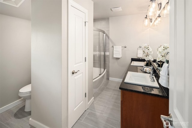 bathroom with double vanity, toilet, baseboards, and combined bath / shower with glass door