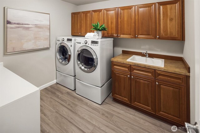 clothes washing area featuring washing machine and dryer, cabinet space, and light wood-type flooring