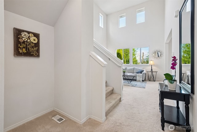 stairs featuring carpet floors, baseboards, a towering ceiling, and visible vents