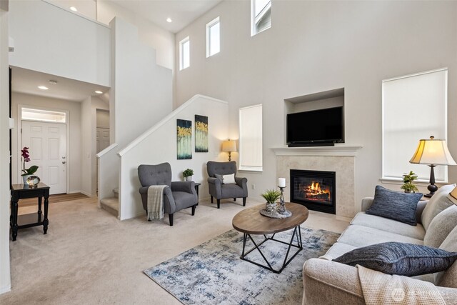 living room featuring stairs, a towering ceiling, light colored carpet, recessed lighting, and a tiled fireplace