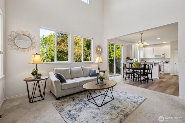 living room with baseboards, a high ceiling, light colored carpet, and a notable chandelier