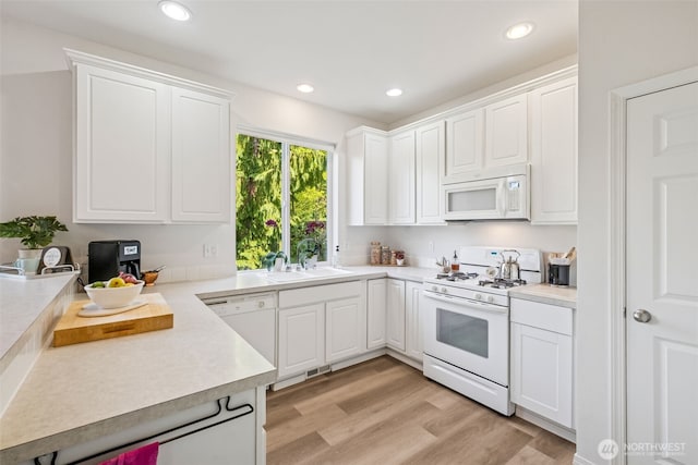 kitchen featuring white cabinets, a sink, light wood finished floors, white appliances, and light countertops