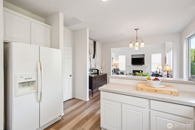 kitchen featuring white refrigerator with ice dispenser, light countertops, white cabinets, light wood finished floors, and hanging light fixtures