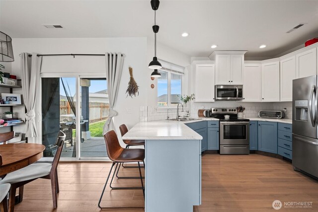 kitchen featuring visible vents, wood finished floors, a peninsula, stainless steel appliances, and white cabinetry