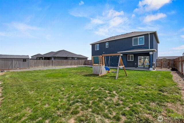 back of house with a playground, an outdoor structure, a yard, and a fenced backyard