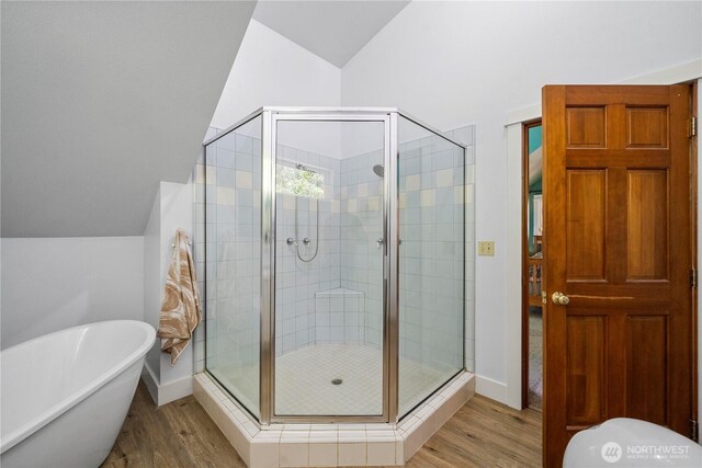 full bath with wood finished floors, vaulted ceiling, a shower stall, a soaking tub, and baseboards
