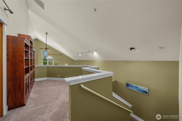hall with an upstairs landing, carpet flooring, vaulted ceiling, baseboards, and track lighting