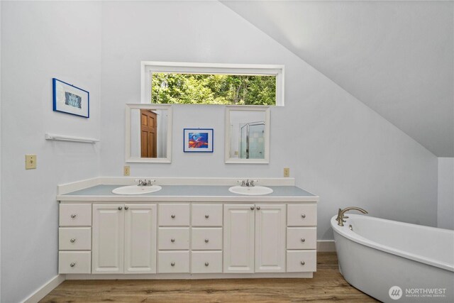 bathroom featuring lofted ceiling, wood finished floors, double vanity, a freestanding bath, and baseboards