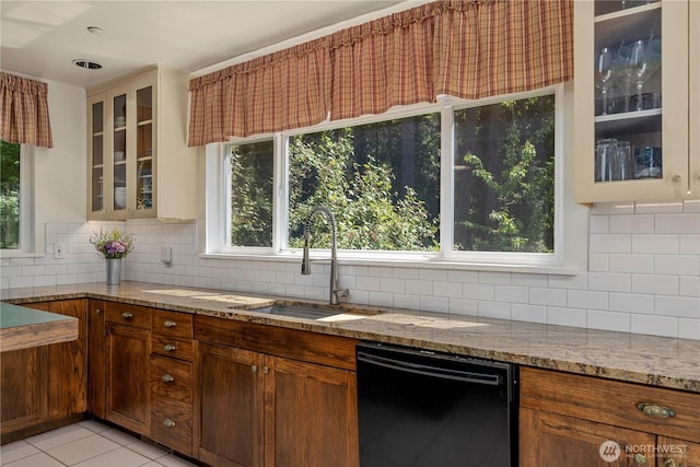 kitchen with black dishwasher, a sink, light stone counters, decorative backsplash, and plenty of natural light