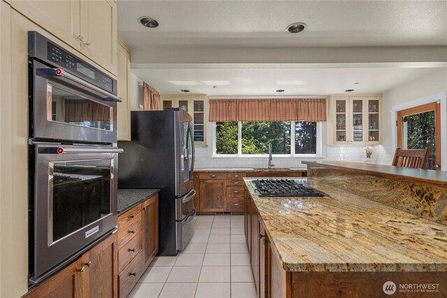 kitchen featuring appliances with stainless steel finishes, tasteful backsplash, a sink, and glass insert cabinets
