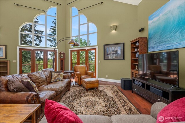 living room with a towering ceiling, french doors, baseboards, and wood finished floors