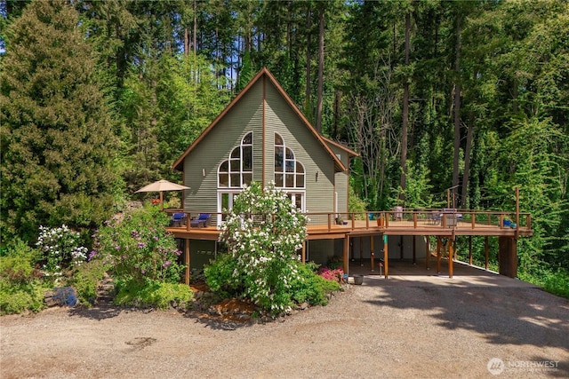 rear view of house with a deck, dirt driveway, a carport, and a forest view