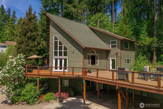 rear view of property featuring a deck, roof with shingles, and a patio