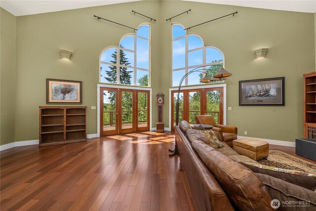 living room featuring french doors, a high ceiling, baseboards, and wood finished floors