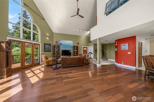 living area featuring a high ceiling, ceiling fan, wood finished floors, stairs, and baseboards