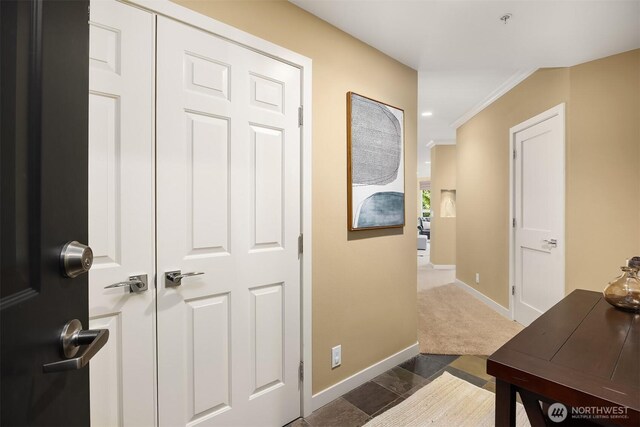 hallway featuring crown molding, baseboards, and dark carpet
