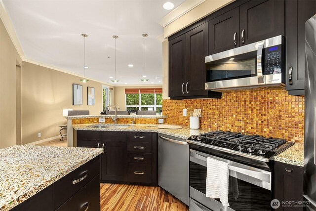kitchen with decorative backsplash, appliances with stainless steel finishes, light wood-type flooring, a sink, and a peninsula