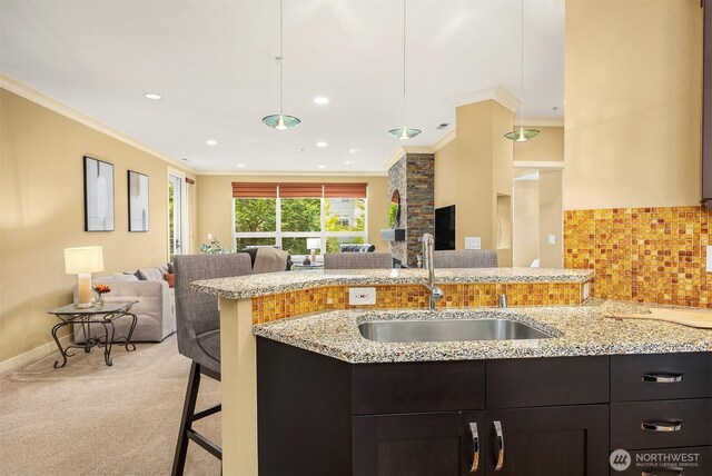 kitchen featuring crown molding, open floor plan, light stone counters, and a sink