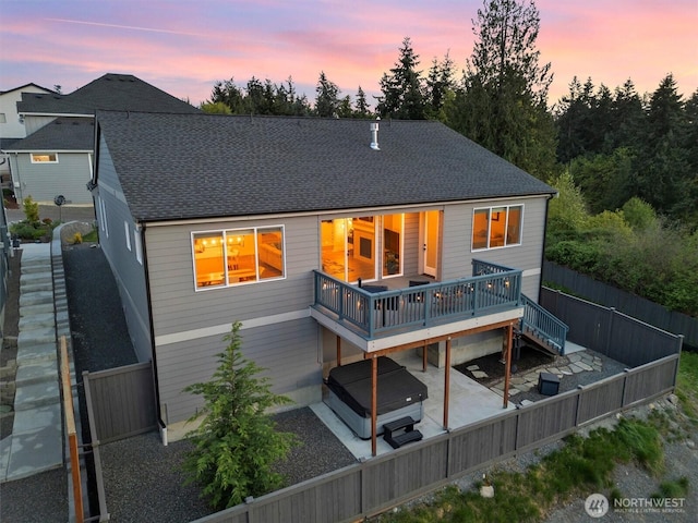 back of property at dusk with fence private yard, a wooden deck, a shingled roof, a patio area, and a hot tub