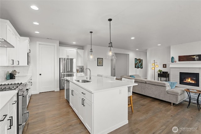 kitchen with a sink, open floor plan, a breakfast bar, stainless steel appliances, and recessed lighting