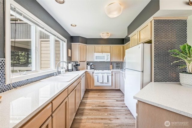 kitchen featuring white appliances, light brown cabinets, a sink, tasteful backsplash, and light stone countertops