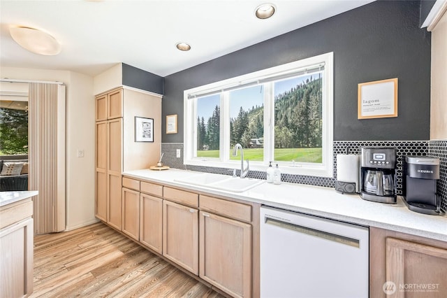 kitchen featuring white dishwasher, a sink, light brown cabinetry, light wood-style floors, and light countertops