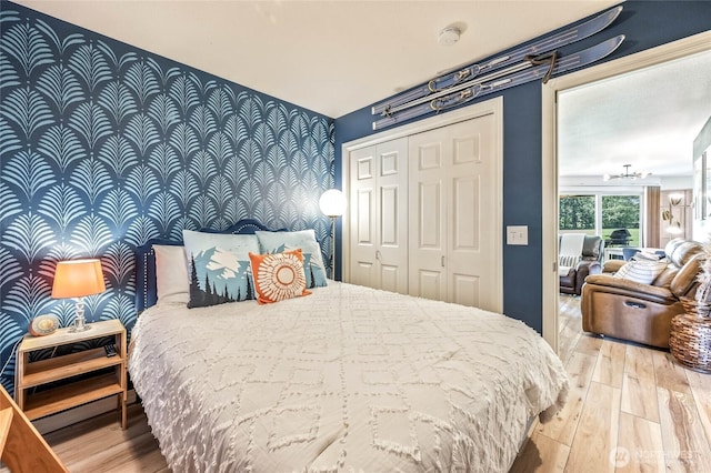bedroom with wallpapered walls, an accent wall, hardwood / wood-style flooring, and a closet