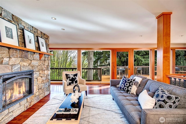 living room featuring wood finished floors, a healthy amount of sunlight, and a stone fireplace