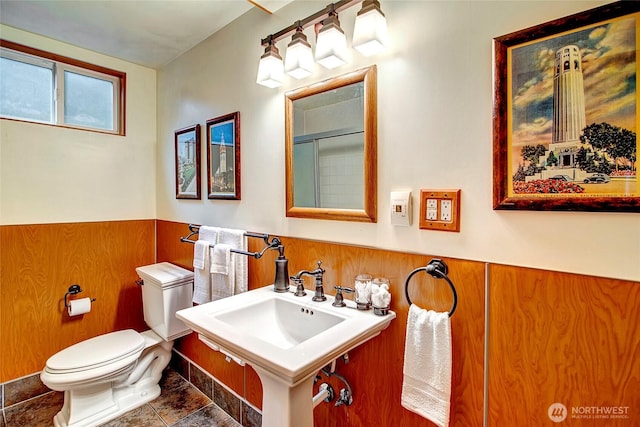 bathroom with a sink, wood walls, an enclosed shower, toilet, and wainscoting