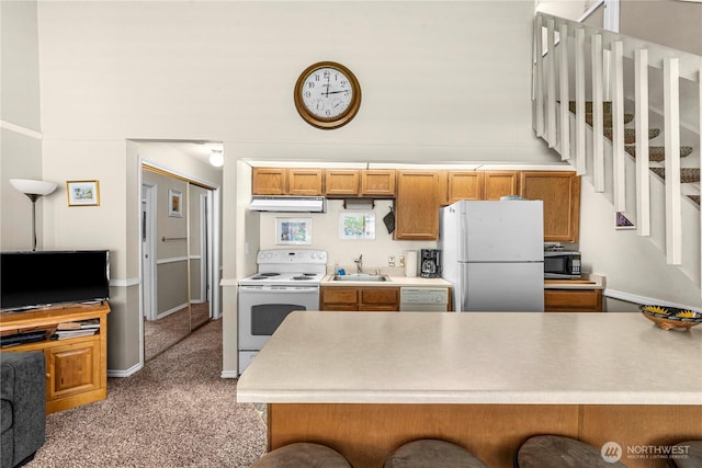 kitchen featuring under cabinet range hood, white appliances, a sink, light carpet, and light countertops