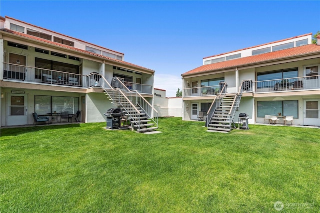 rear view of house featuring stairs, stucco siding, and a lawn